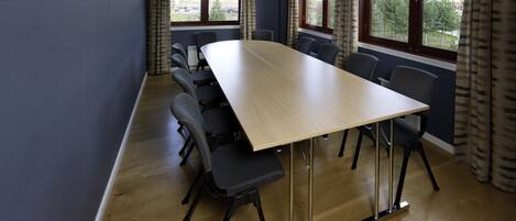 Un salón de conferencias con una mesa larga, sillas y ventanas grandes con cortinas.