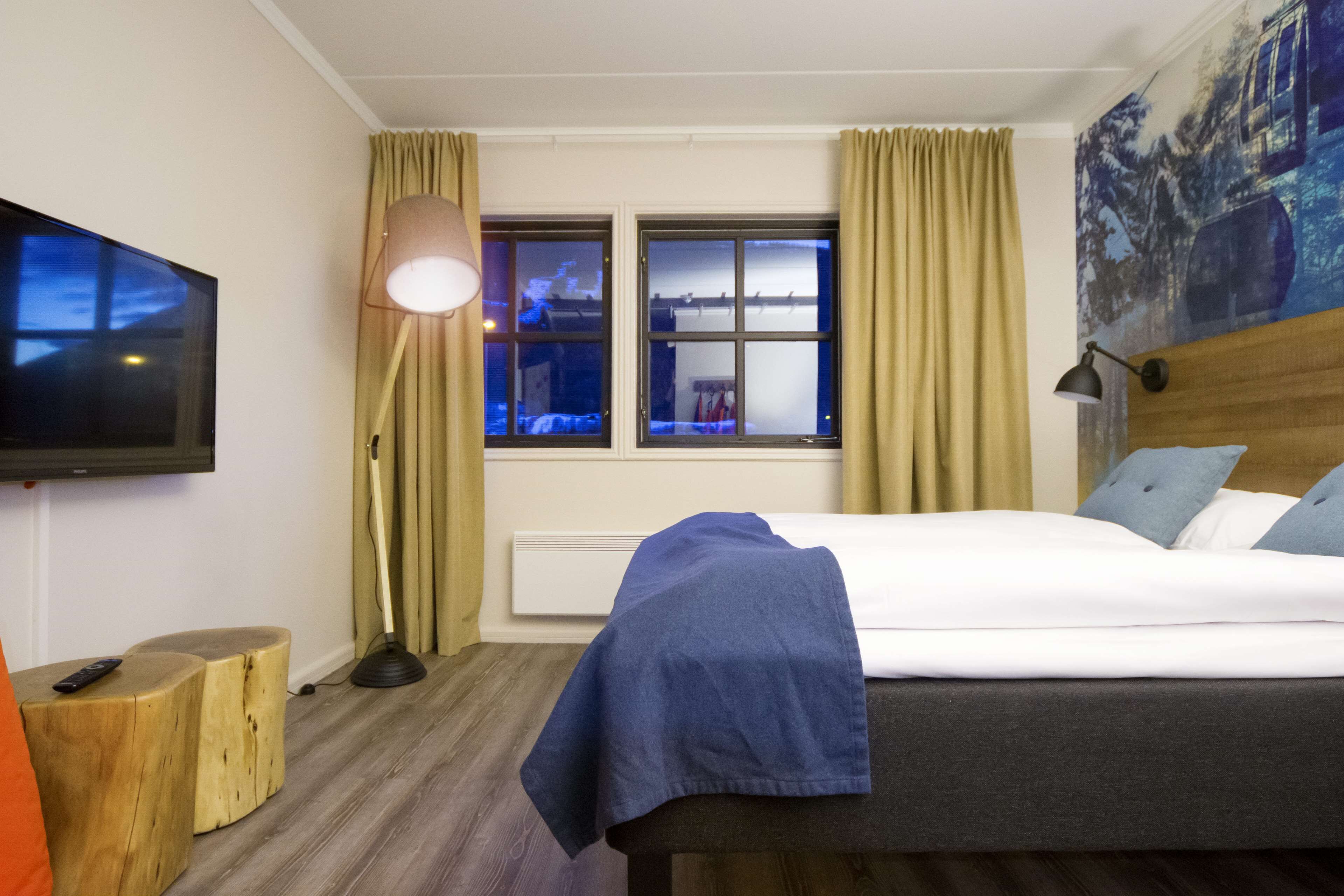 Habitación de hotel con cama, televisor de pantalla plana en la pared, ventana con cortinas y un cuadro en la pared.