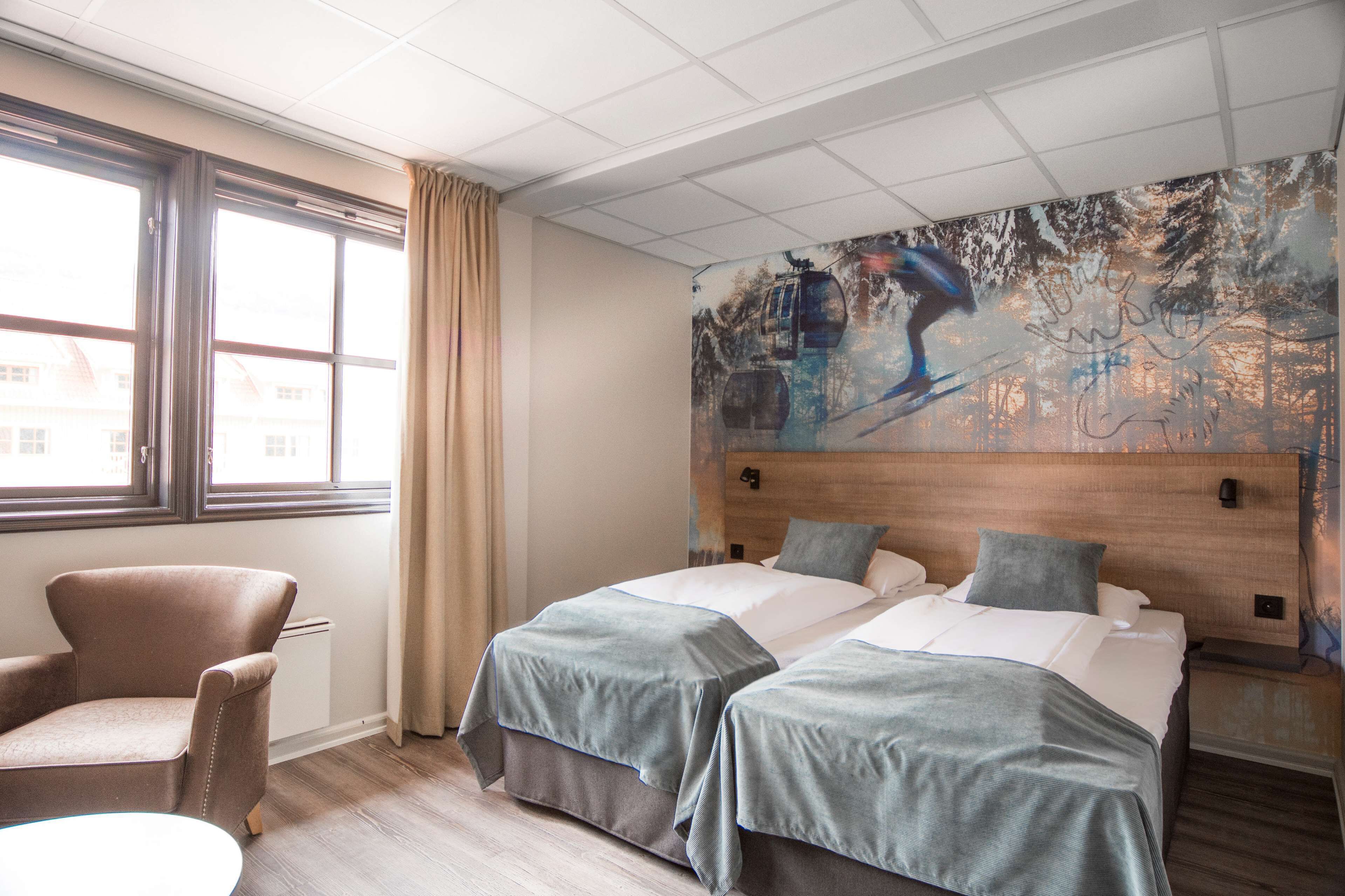 Habitación de hotel con dos camas, una silla, una mesa redonda y un ventanal grande.