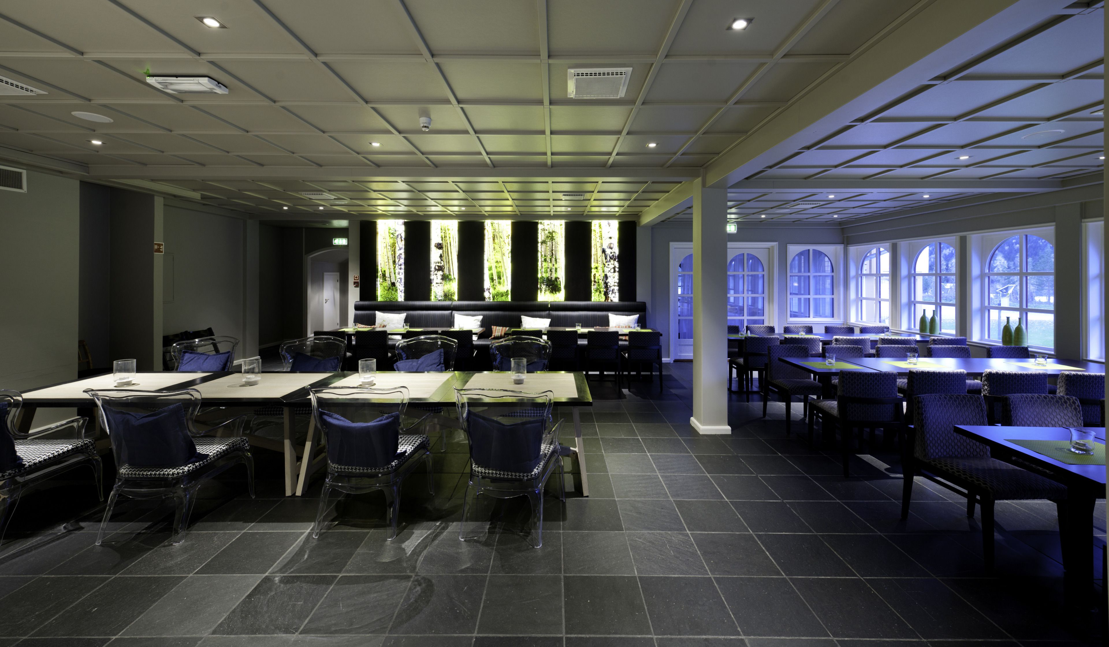 Un comedor moderno con varias mesas y sillas, ventanas amplias e iluminación empotrada en el techo.