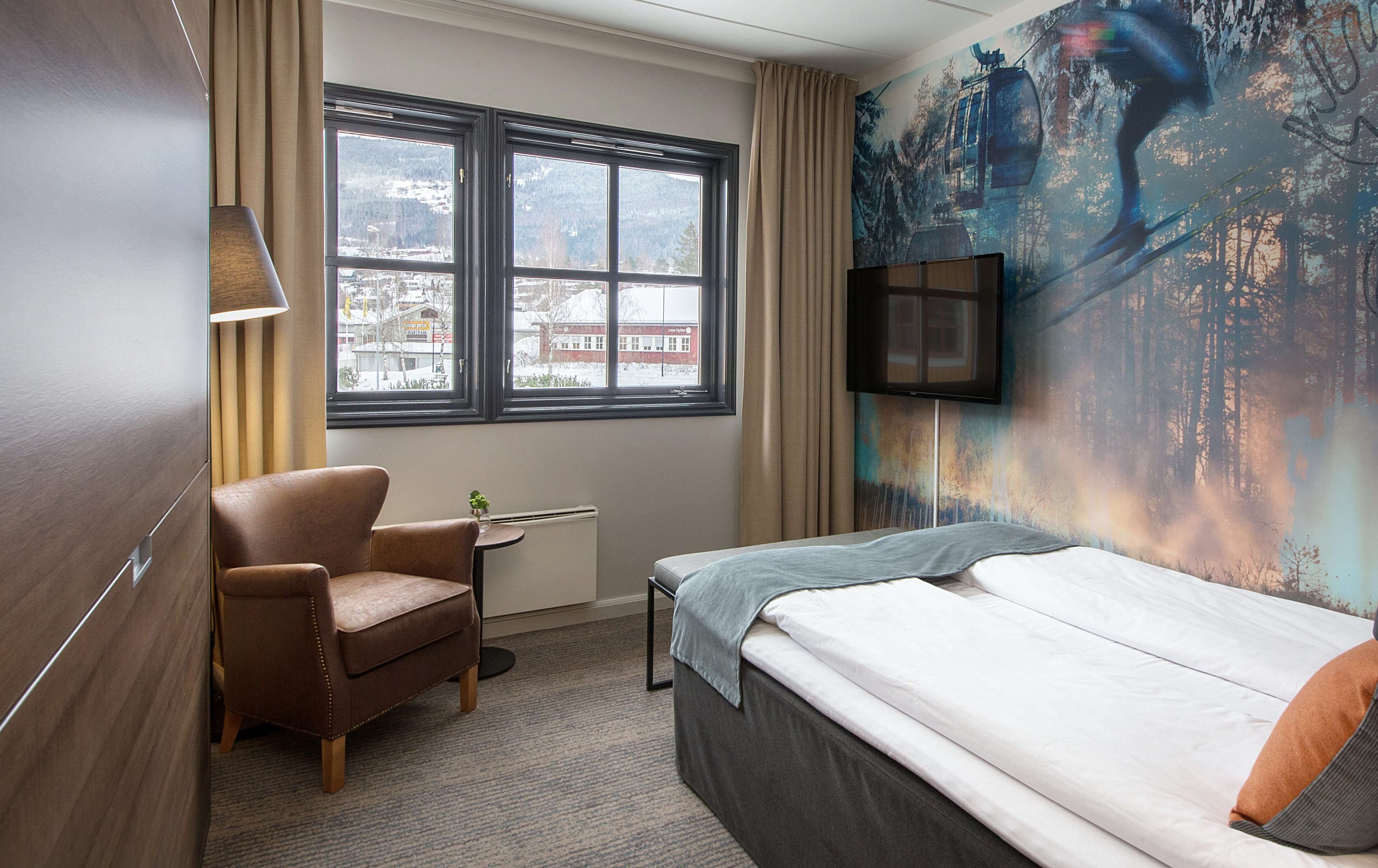 Une chambre d’hôtel avec un lit, une chaise, un bureau, une télévision et une fenêtre donnant sur un paysage enneigé.