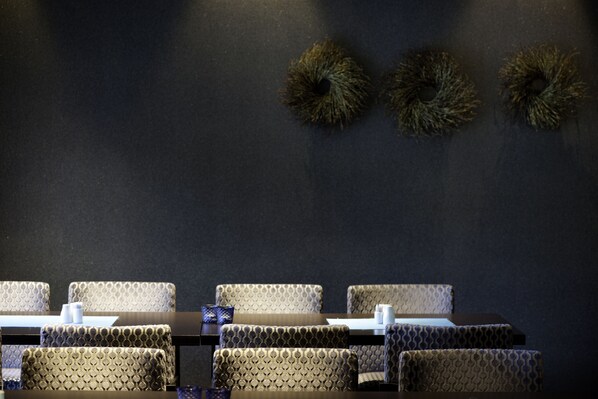 Un salón de conferencias con pared oscura, sillas estampadas y una mesa con mantel blanco.