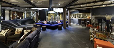 A modern lobby with a blue sofa, a fireplace, and a bar area.