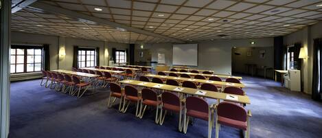 A conference room with rows of tables and chairs, a projector screen, and a whiteboard.
