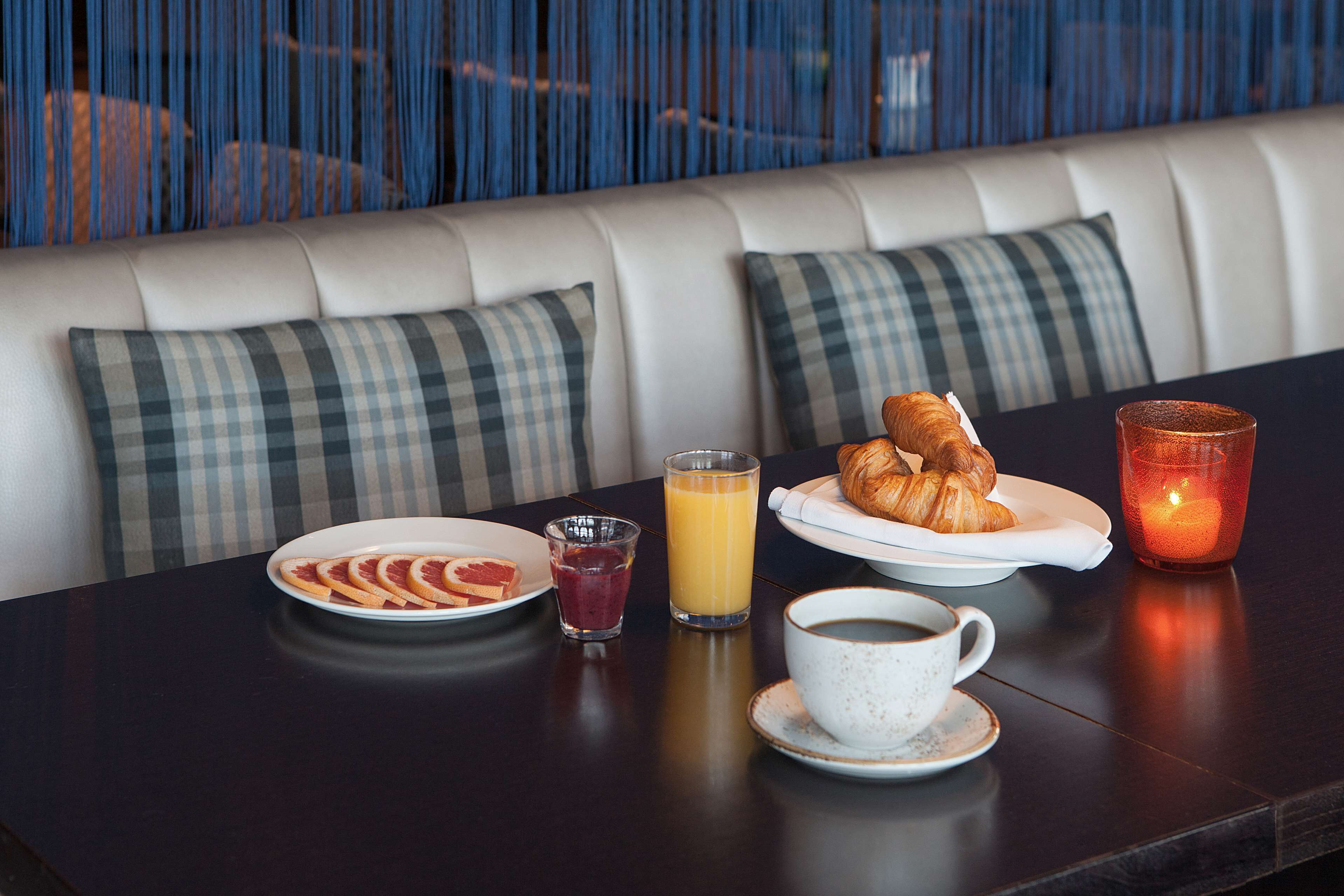 Et morgenbord med et fad croissanter, et glas appelsinjuice, en kop kaffe og et lys på et bord.
