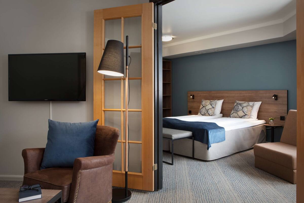 Una habitación de hotel con cama, escritorio, silla, televisor y armario.