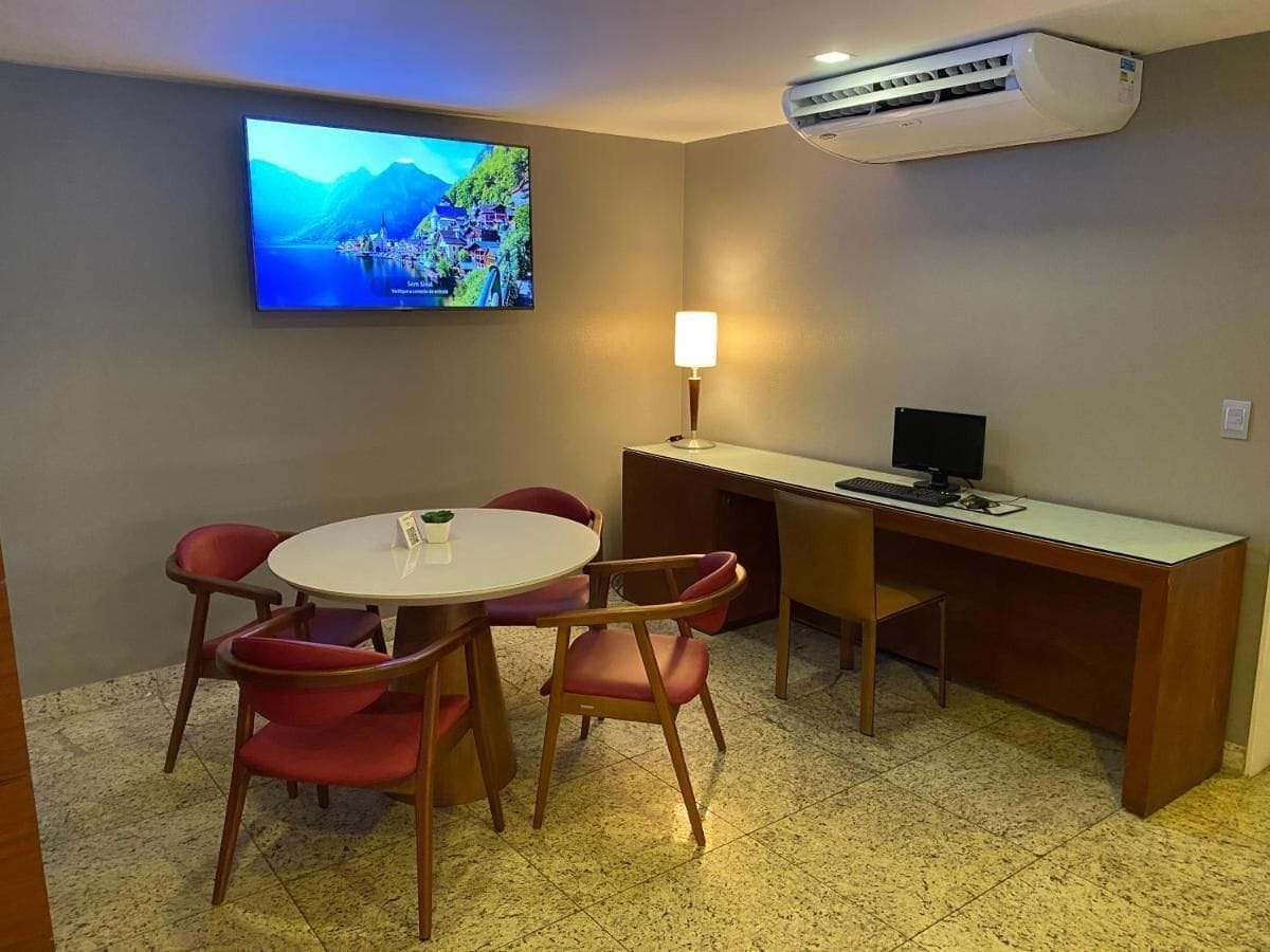 Una sala de reuniones pequeña con una mesa redonda, sillas rojas, un escritorio con una computadora, un televisor instalado en la pared y un equipo de aire acondicionado.