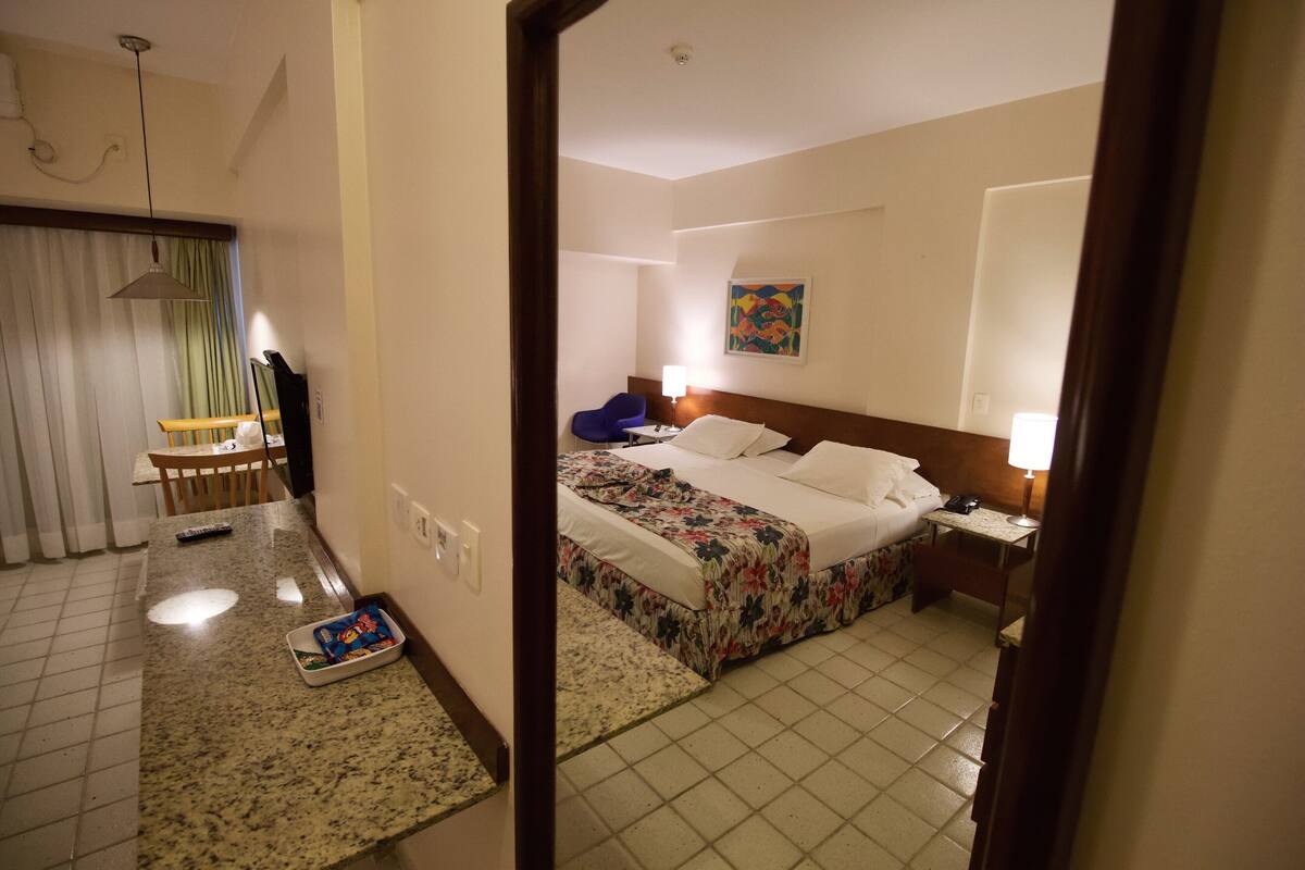 A hotel room with a bed, bedside table, lamp, and a painting on the wall.