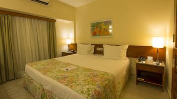 Quarto de hotel com uma cama grande, duas mesas de cabeceira com abajures, um quadro na parede e uma janela com cortinas.