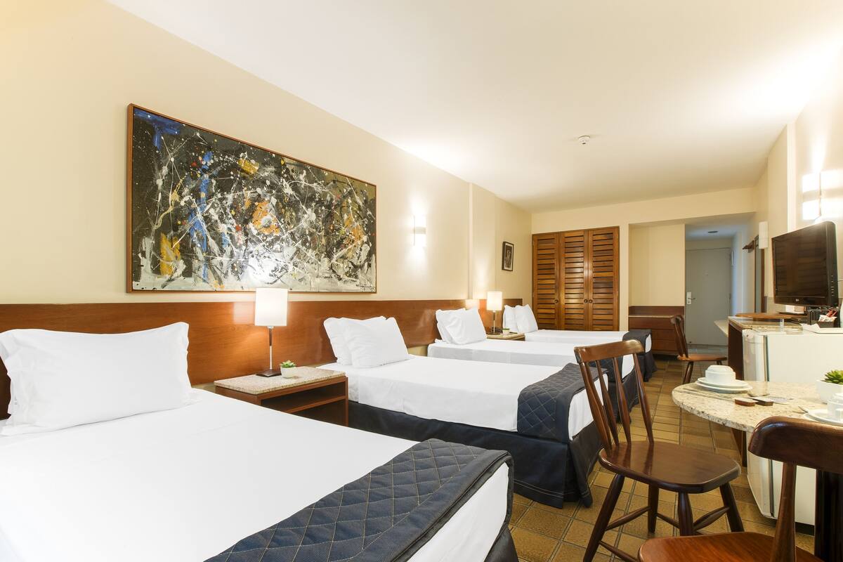 A hotel room with three beds, a dining area, and a TV.