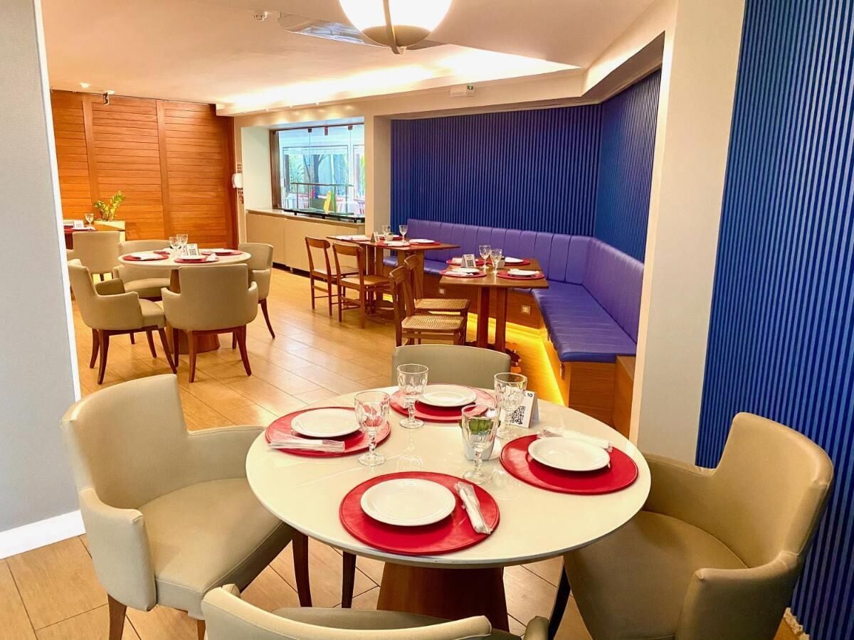 Un comedor con mesas redondas dispuestas para cuatro personas, sillas color beige y un banco acolchado azul.