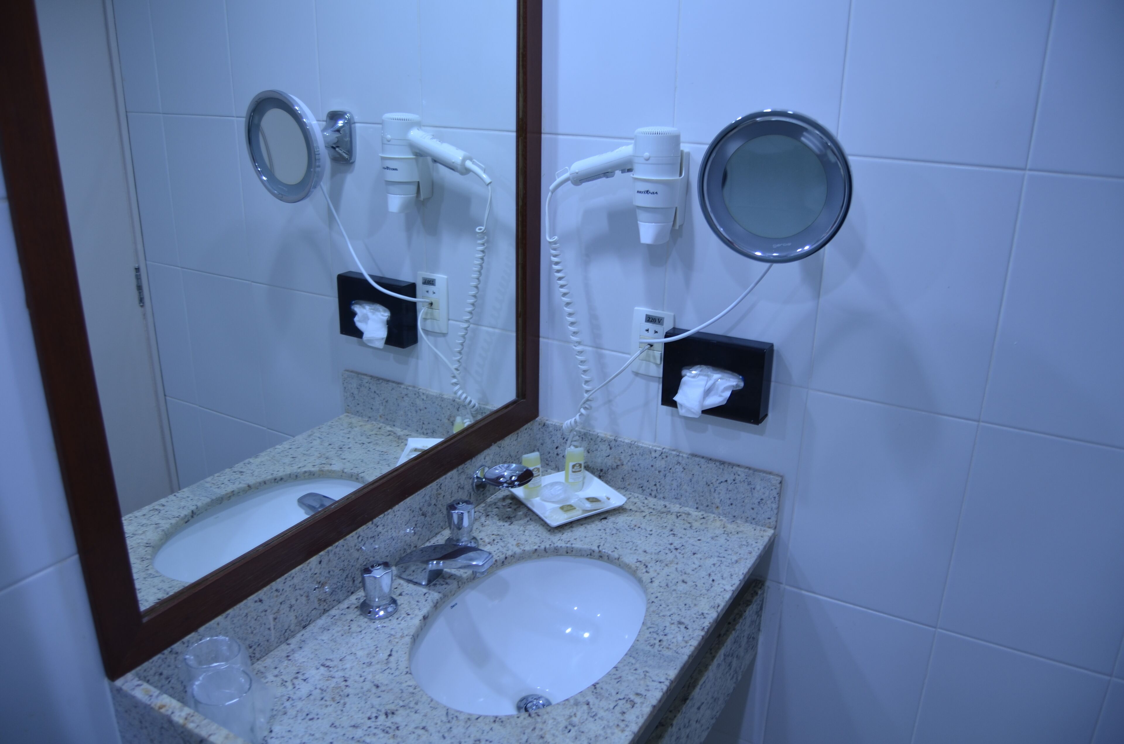 A bathroom with a sink, mirror, hairdryer, and towel dispenser.