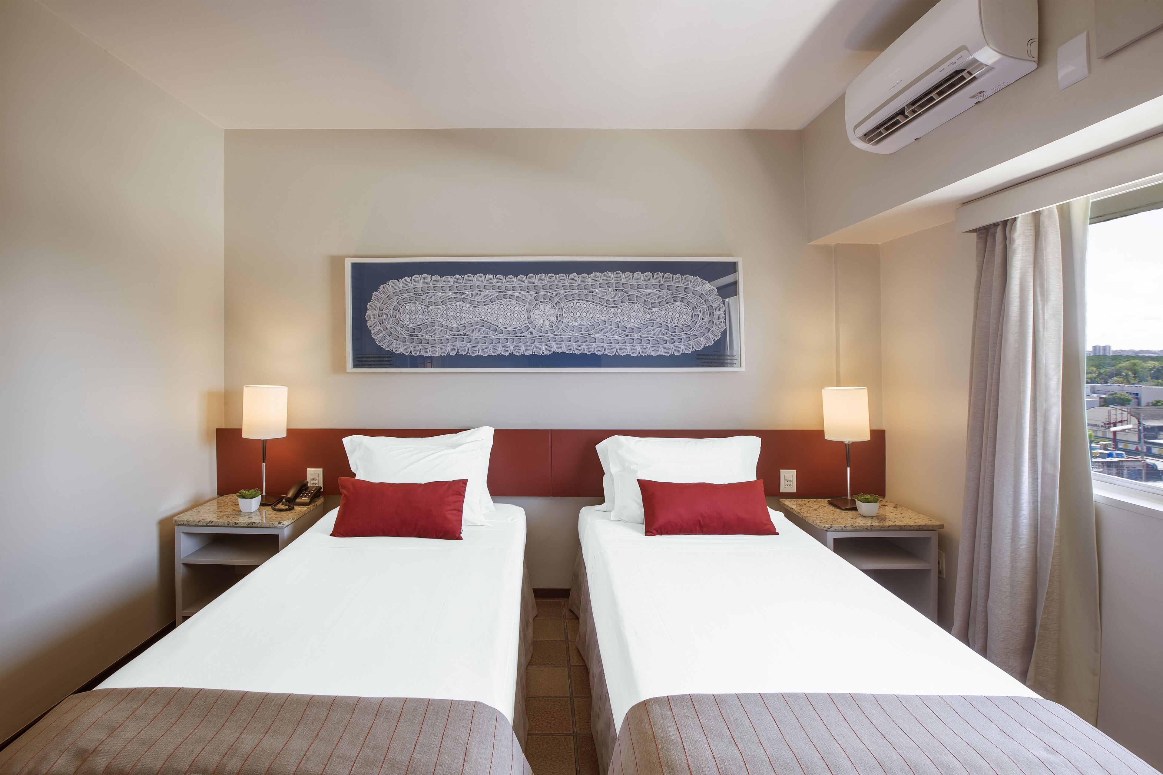 A hotel room with two beds, a large artwork on the wall, and a view of the city through the window.