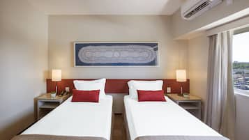 A hotel room with two beds, a large artwork on the wall, and a view of the city through the window.