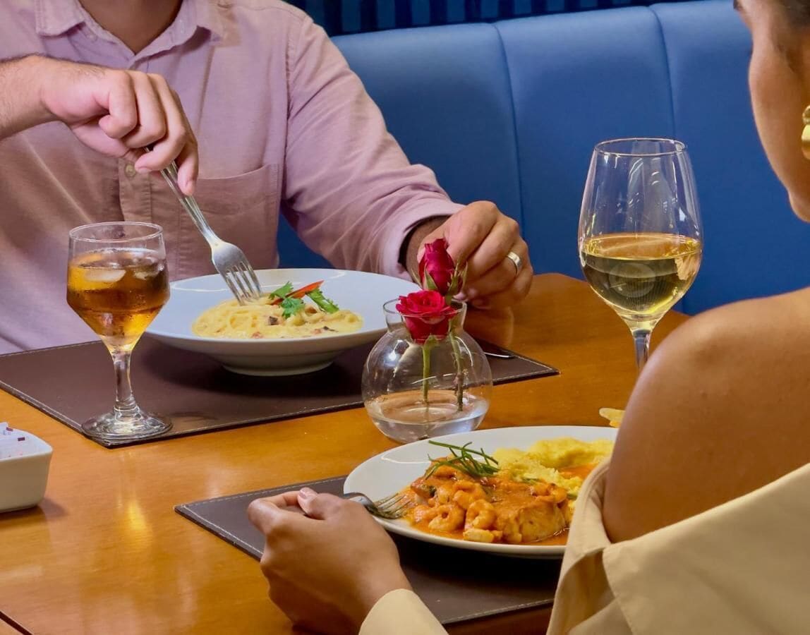 A dining table with two plates of pasta, a glass of white wine, and a glass of beer.