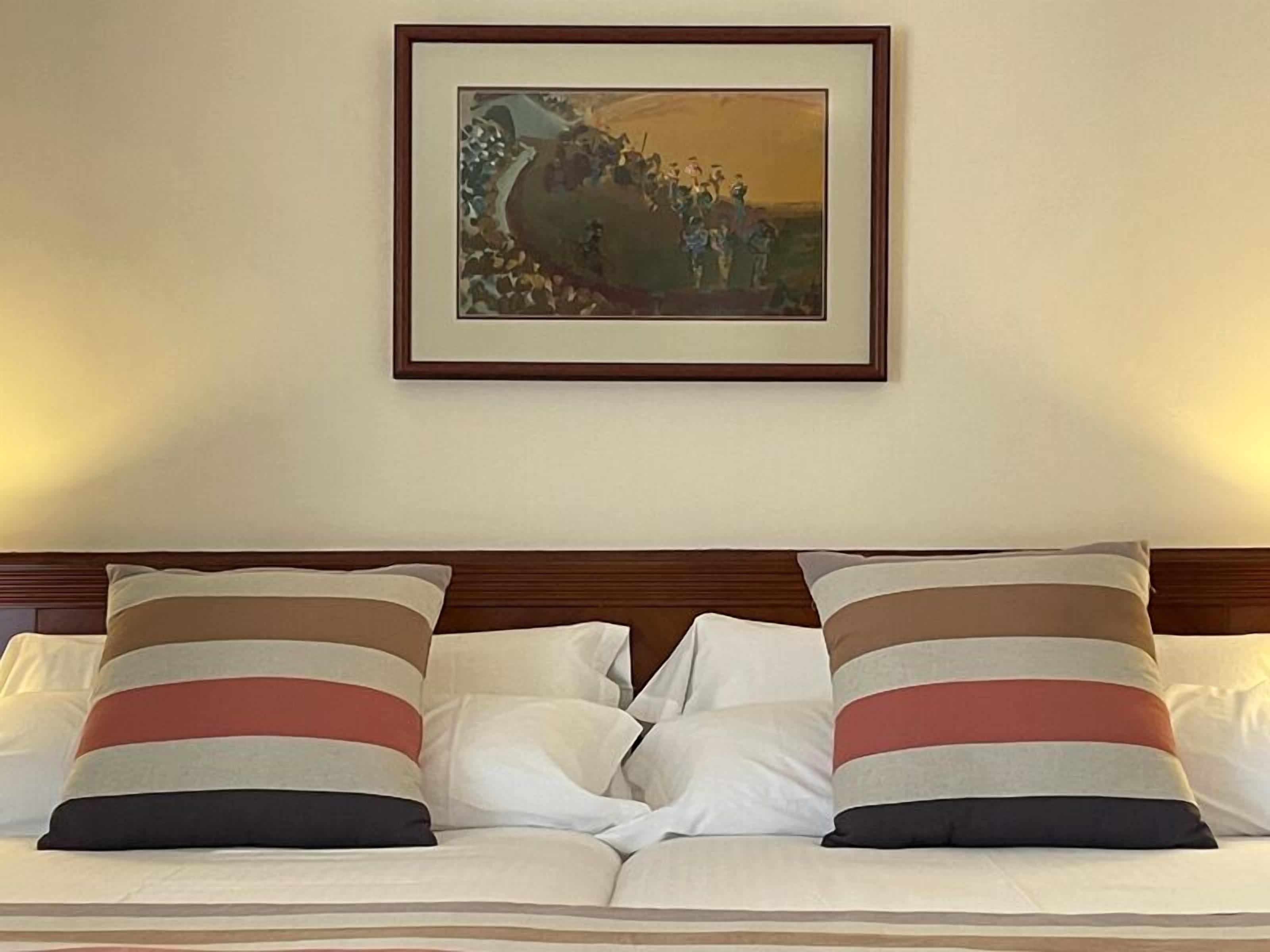 A bed with striped pillows and a framed painting above it.
