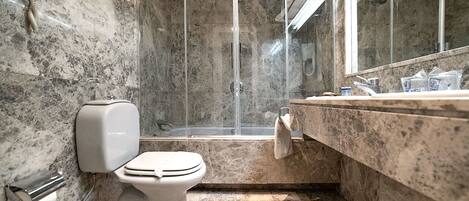 A bathroom with a marble floor, a toilet, a shower enclosure, and a sink with a towel hanging on the wall.