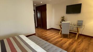 A room with a striped sofa, a desk with a chair, a TV on the wall, and wooden flooring.