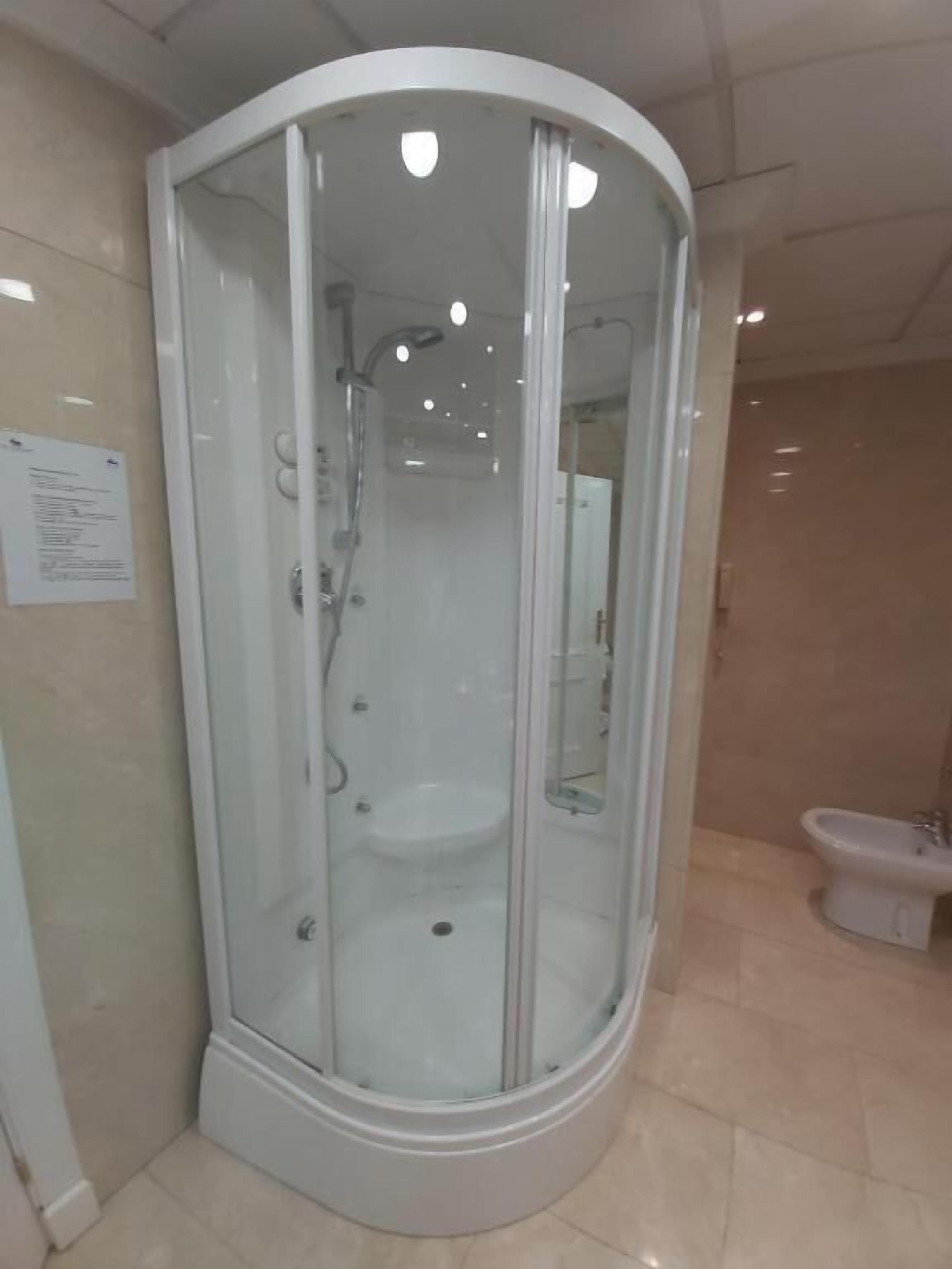 A glass-enclosed shower stall with a white sink and a handheld showerhead.
