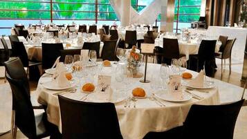 Une salle de banquet avec des tables rondes dressées pour le repas, chacune étant agrémentée de couverts, de verres et d’un présentoir à menus.