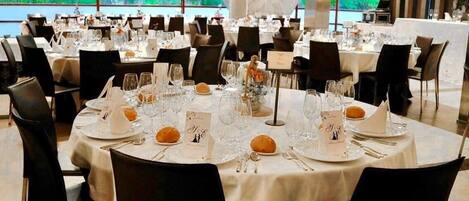 Un salón de banquetes con mesas redondas dispuestas para comer, cada una con vajilla, copas y un atril para el menú.