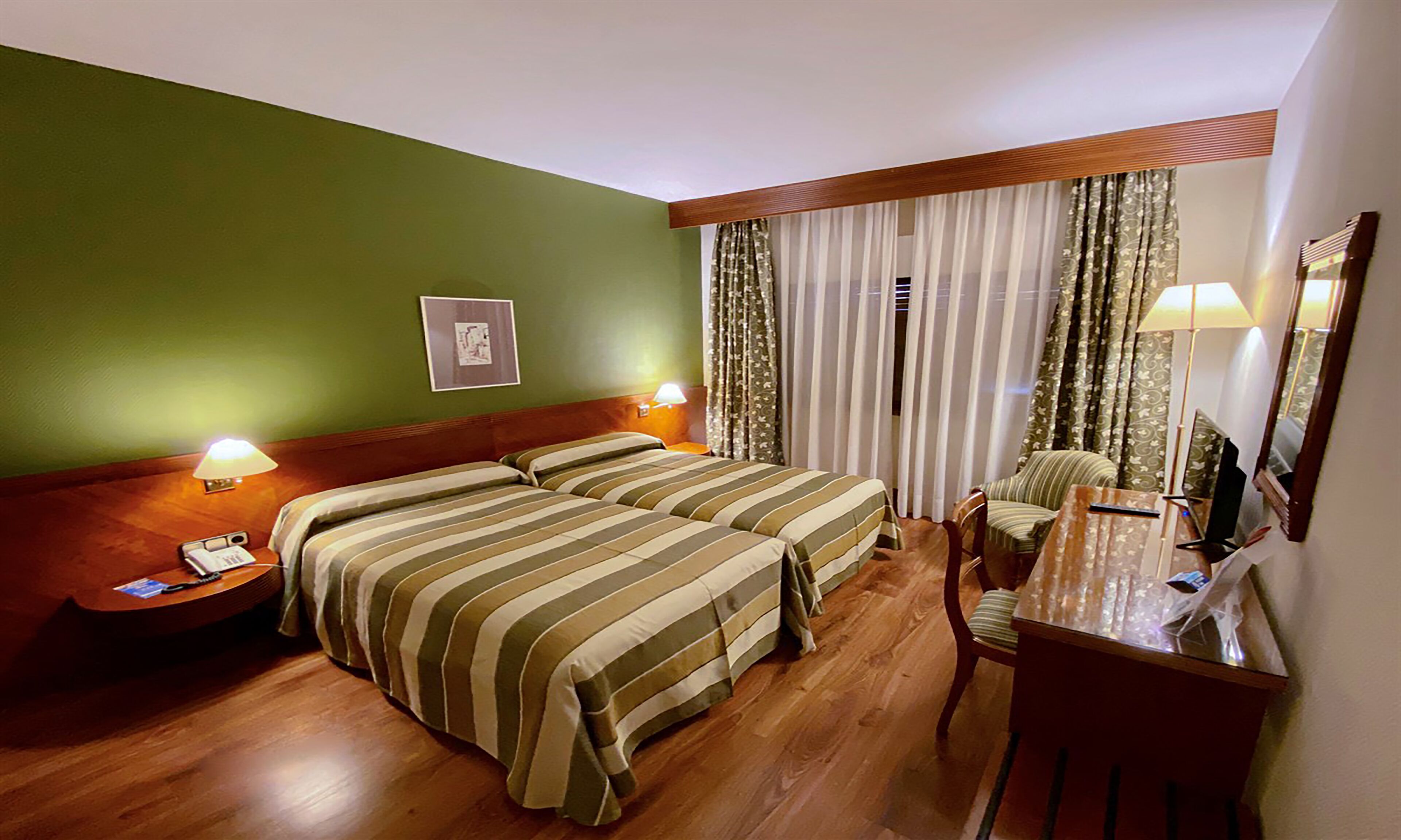 Une chambre d’hôtel avec deux lits, un bureau, une chaise, une lampe et un miroir.
