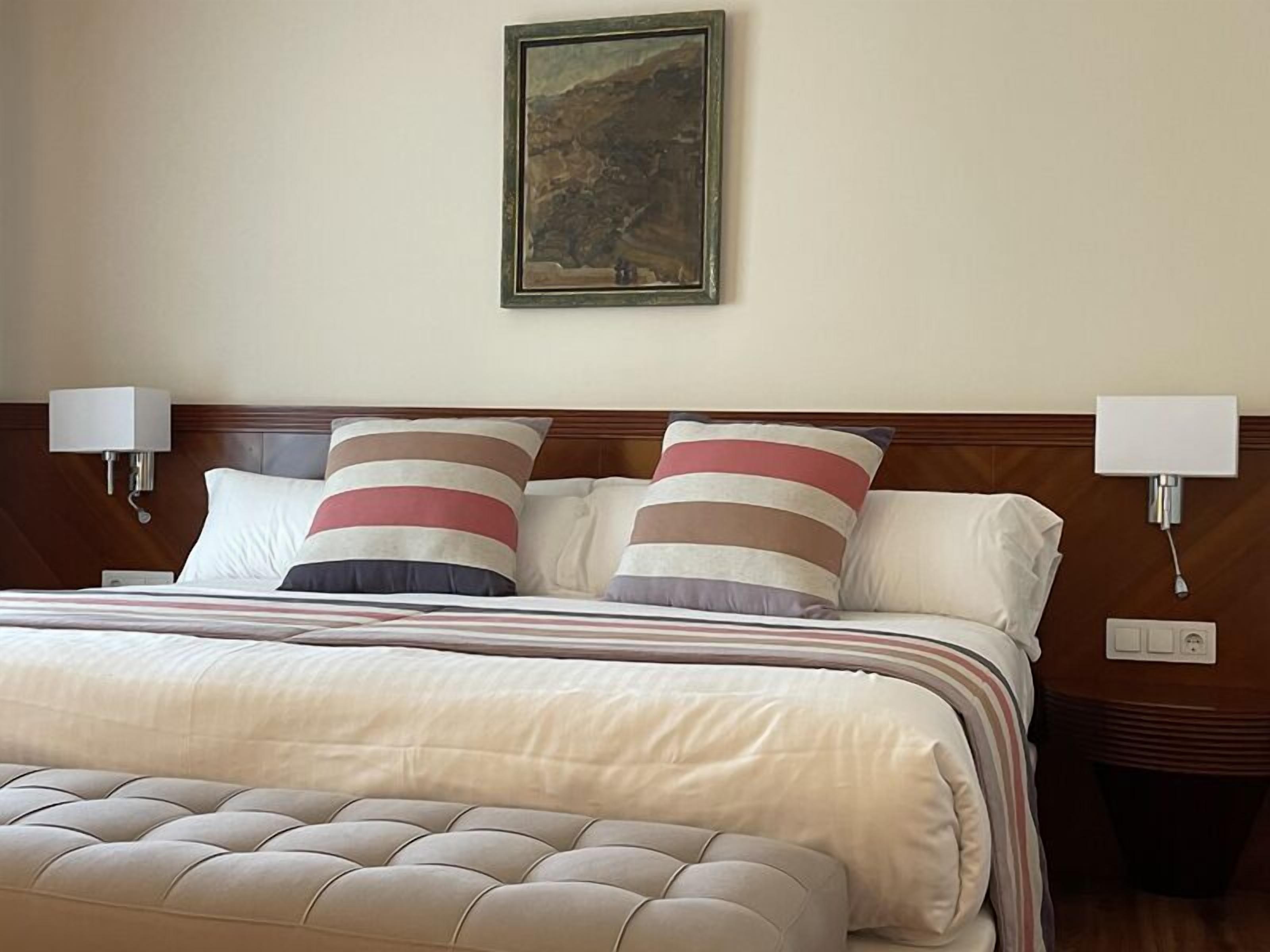 Un cuarto de hotel con una cama grande, dos lámparas de noche y un cuadro en la pared.