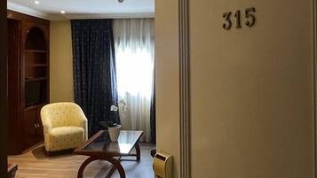 Habitación de hotel con piso de madera, un sillón amarillo, una mesita de centro de vidrio y una puerta con el número 315.