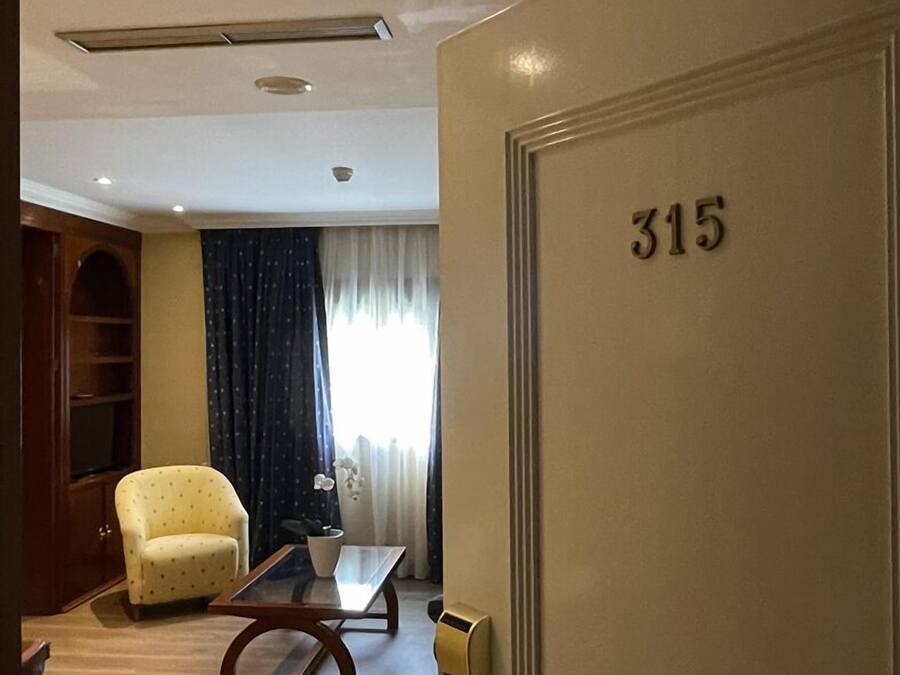 Habitación de hotel con piso de madera, un sillón amarillo, una mesita de centro de vidrio y una puerta con el número 315.