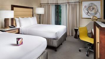 A hotel room with two beds, a desk, a chair, and a large window with curtains.