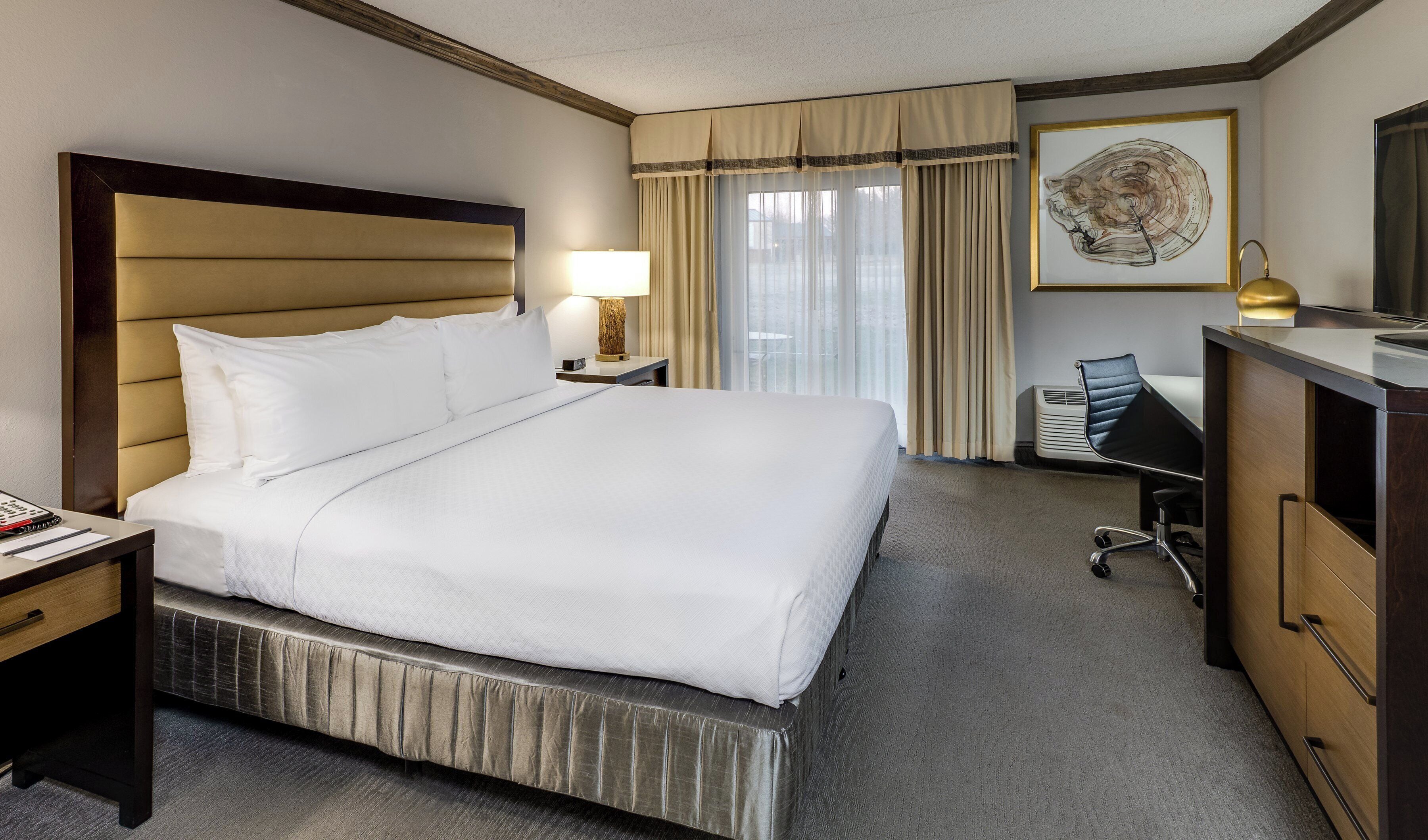 A hotel room with a large bed, a desk, a chair, a dresser, and a window with curtains.