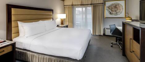 A hotel room with a large bed, a desk, a chair, a dresser, and a window with curtains.