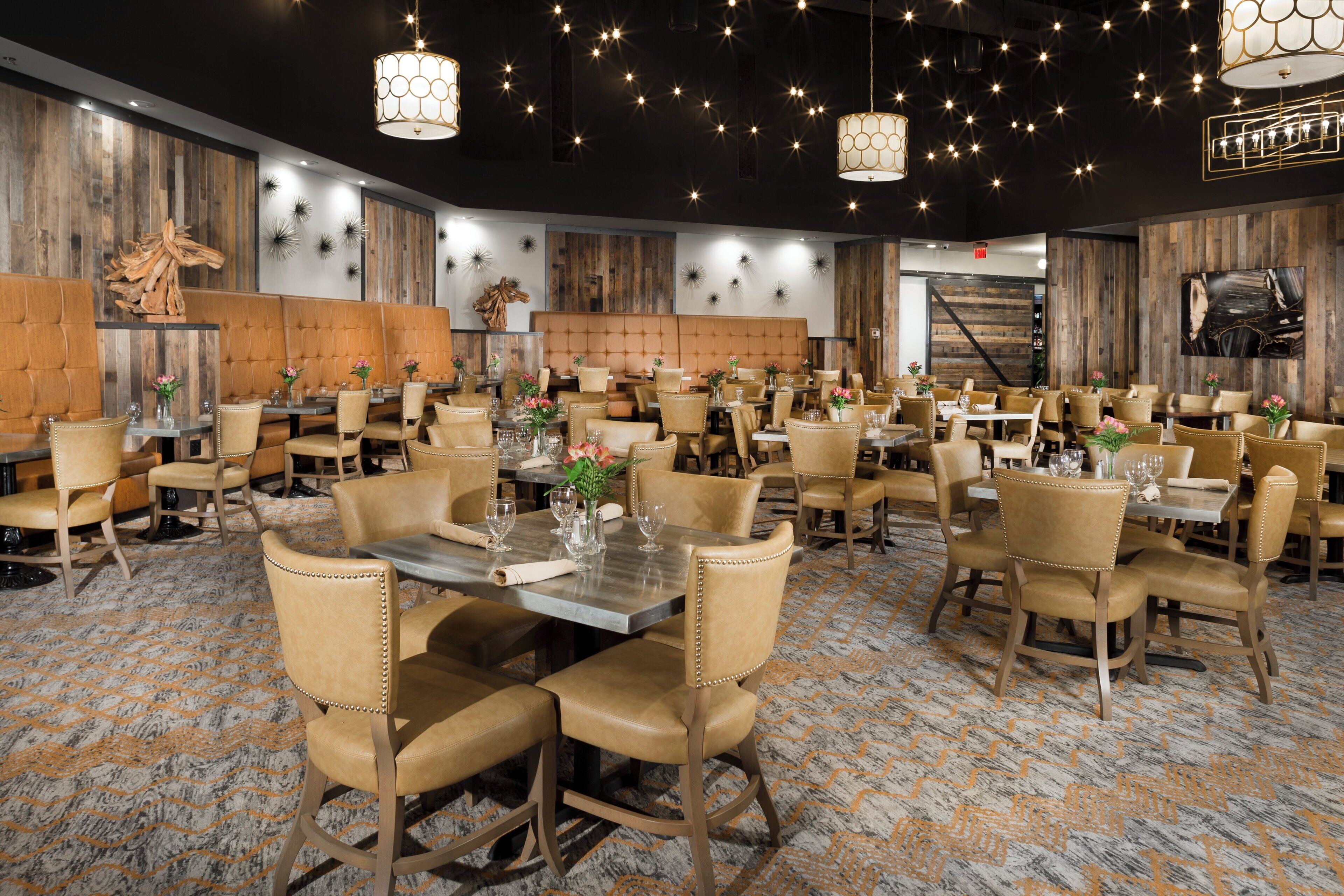 Un comedor amplio con varias mesas y sillas, paneles de madera y lámparas decorativas.