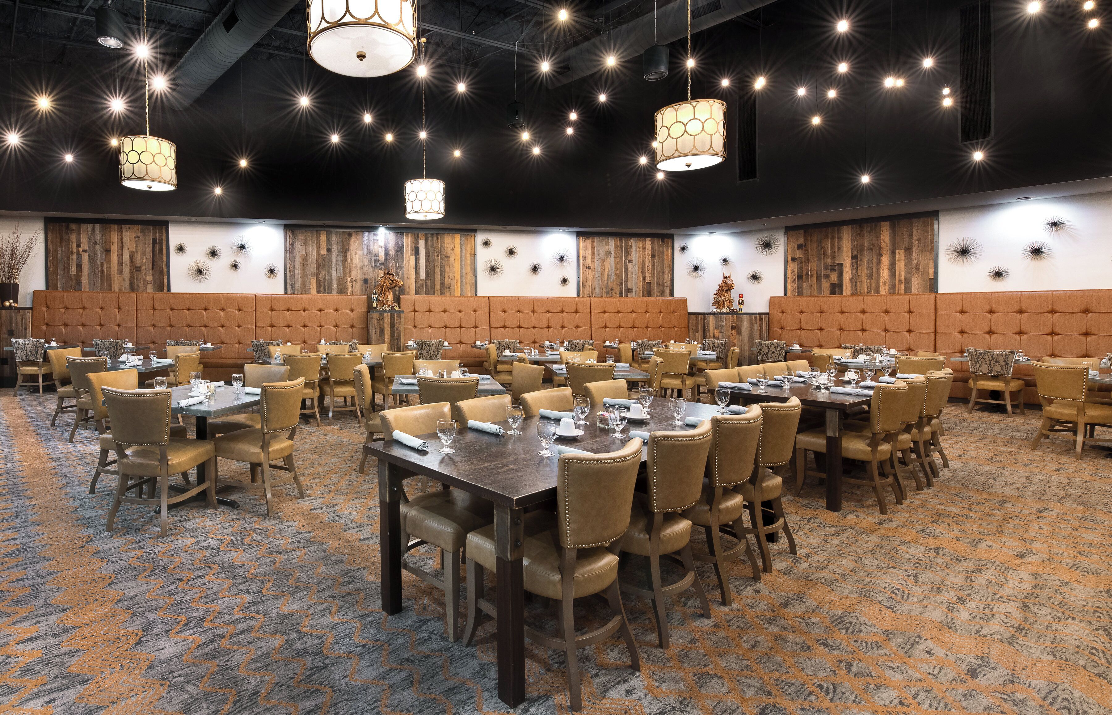A spacious banquet hall with multiple tables and chairs, high ceiling with hanging lights, and decorative wall panels.