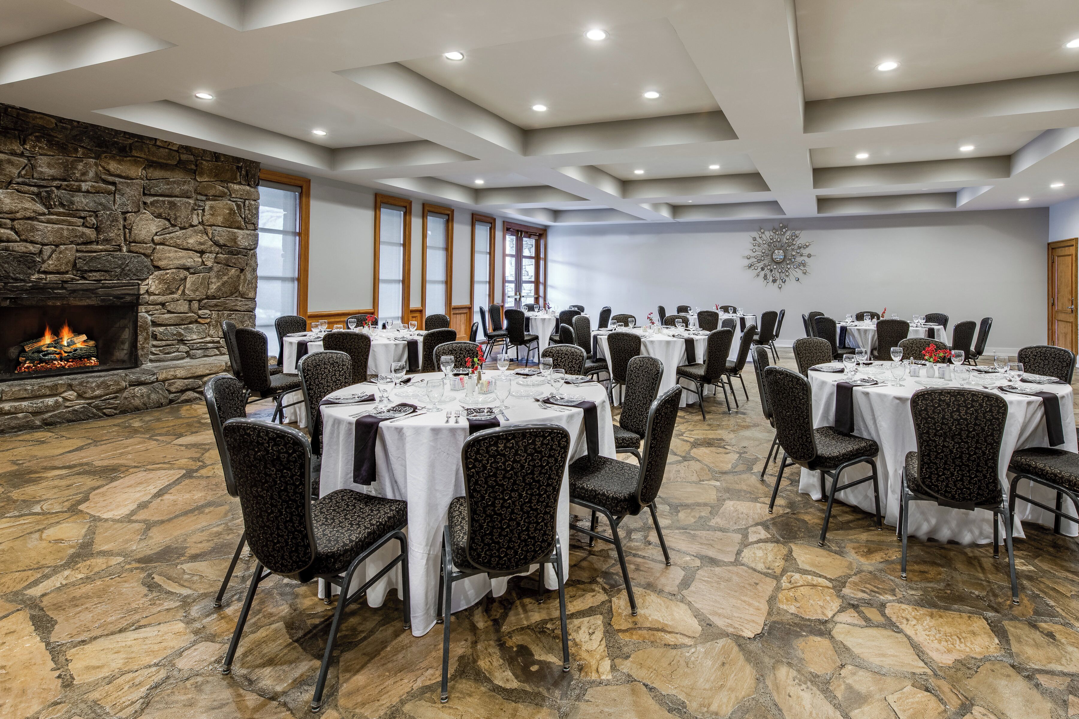 A conference room with round tables, chairs, a stone fireplace, and a decorative wall piece.