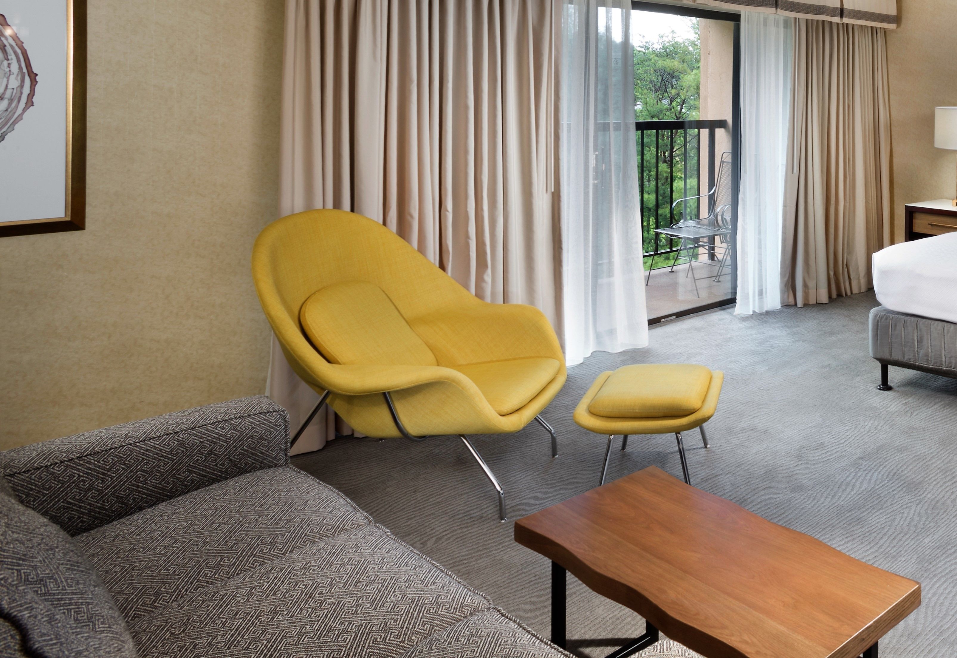 Una habitación de hotel con sofá, un sillón amarillo, una mesa de madera y un balcón con una silla.