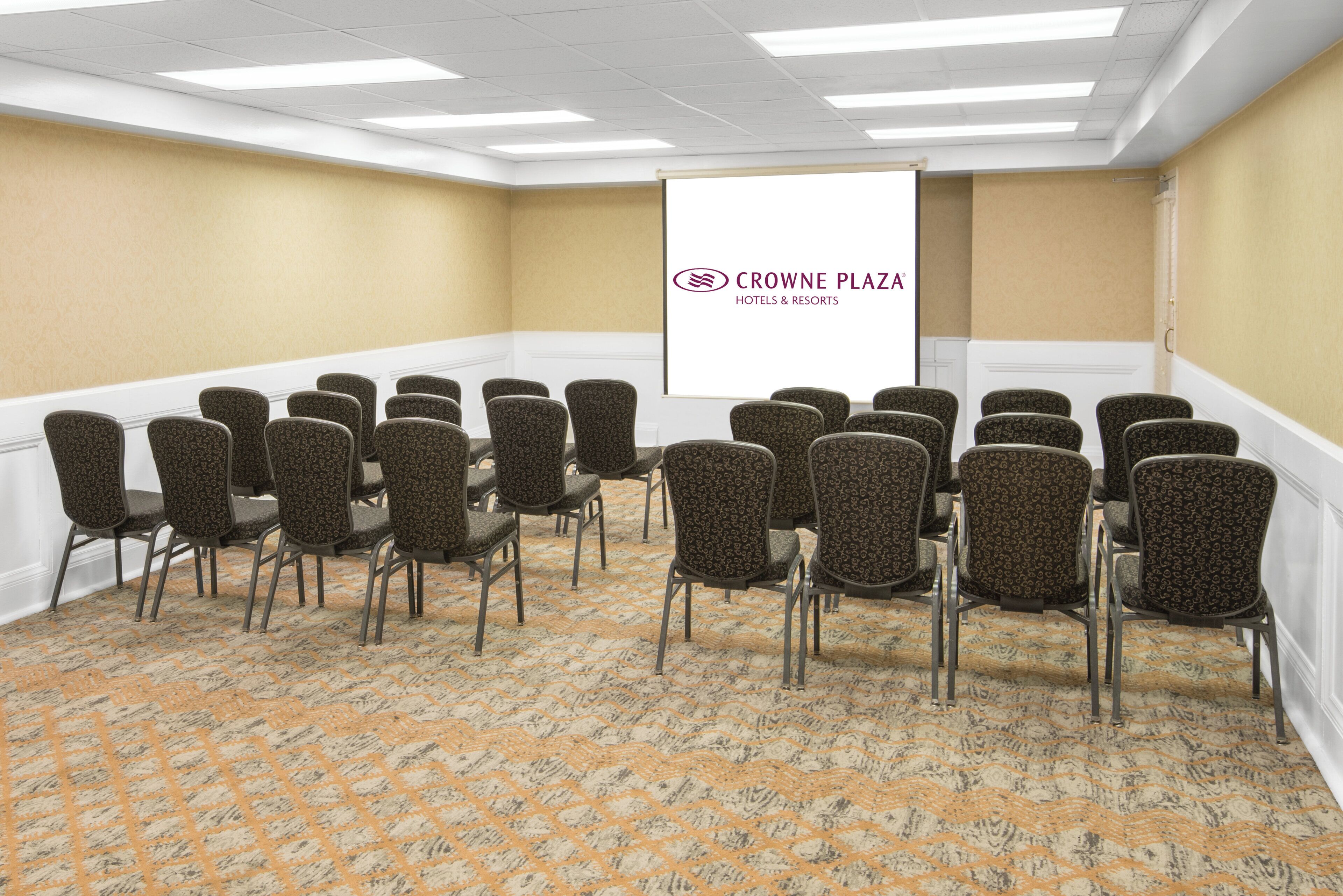 Une salle de conférence avec des rangées de chaises, un écran de projection et un sol recouvert de moquette.
