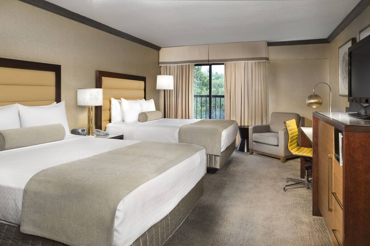 A hotel room with two beds, a desk, a chair, a TV, and a window with curtains.