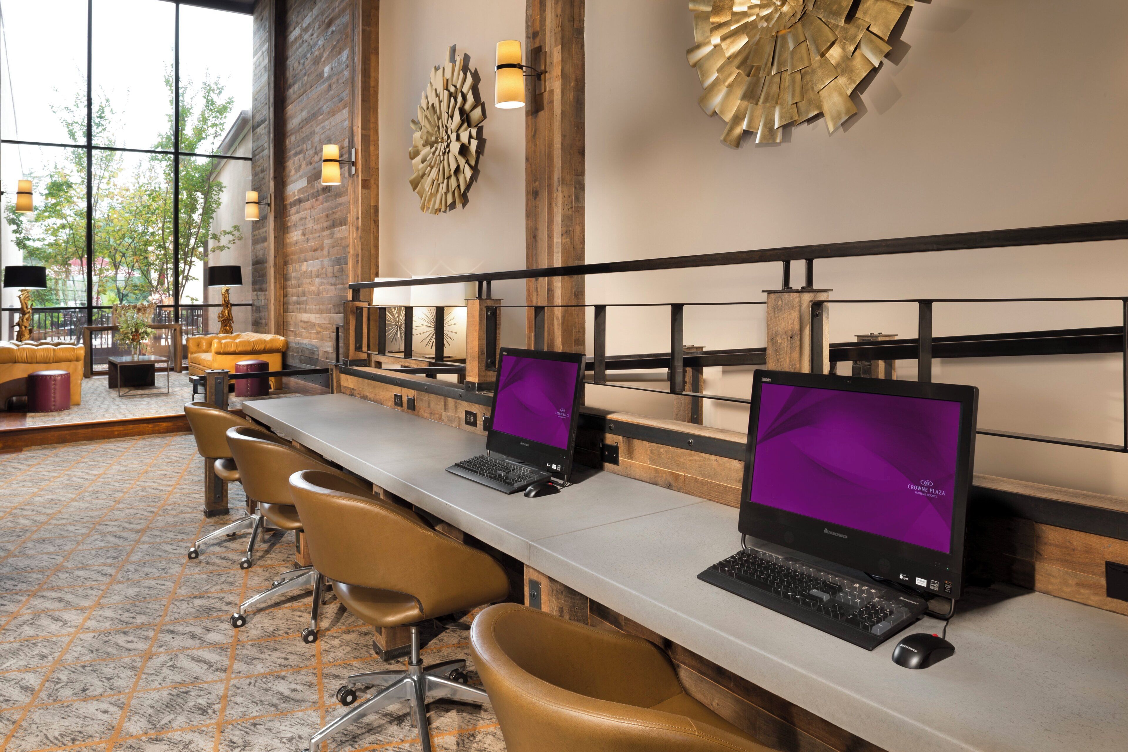 A modern hotel lobby with long tables, leather chairs, and large windows.
