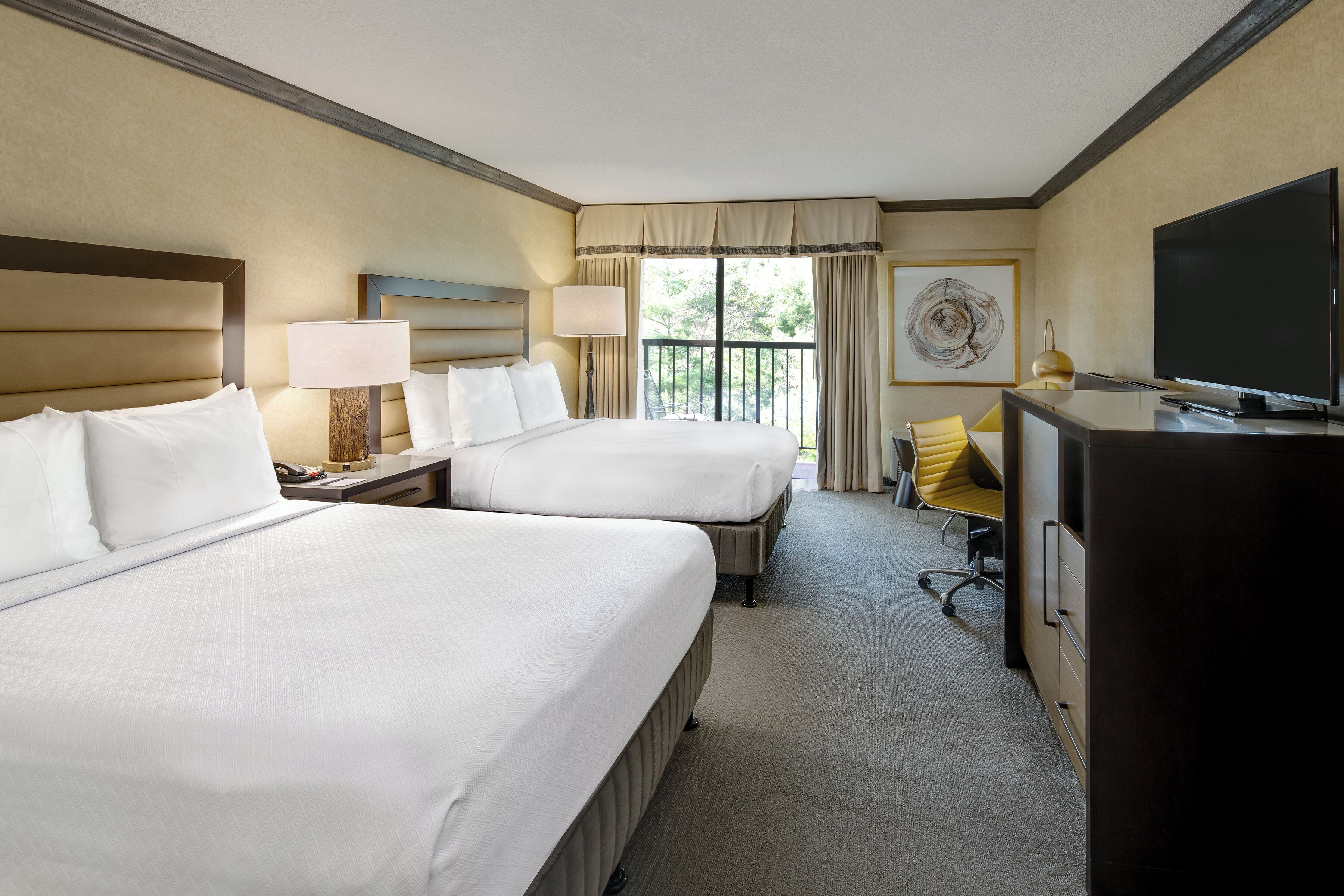 A hotel room with two beds, a desk, a chair, a television, and a window with curtains.