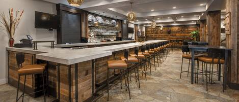 A bar area with a long counter, multiple stools, and hanging pendant lights.