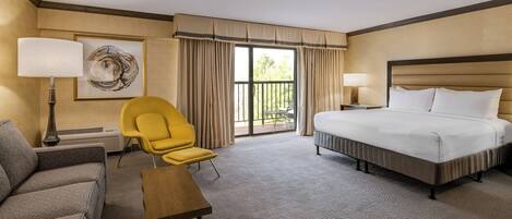 A hotel room with a bed, a chair, a table, a lamp, and a painting.