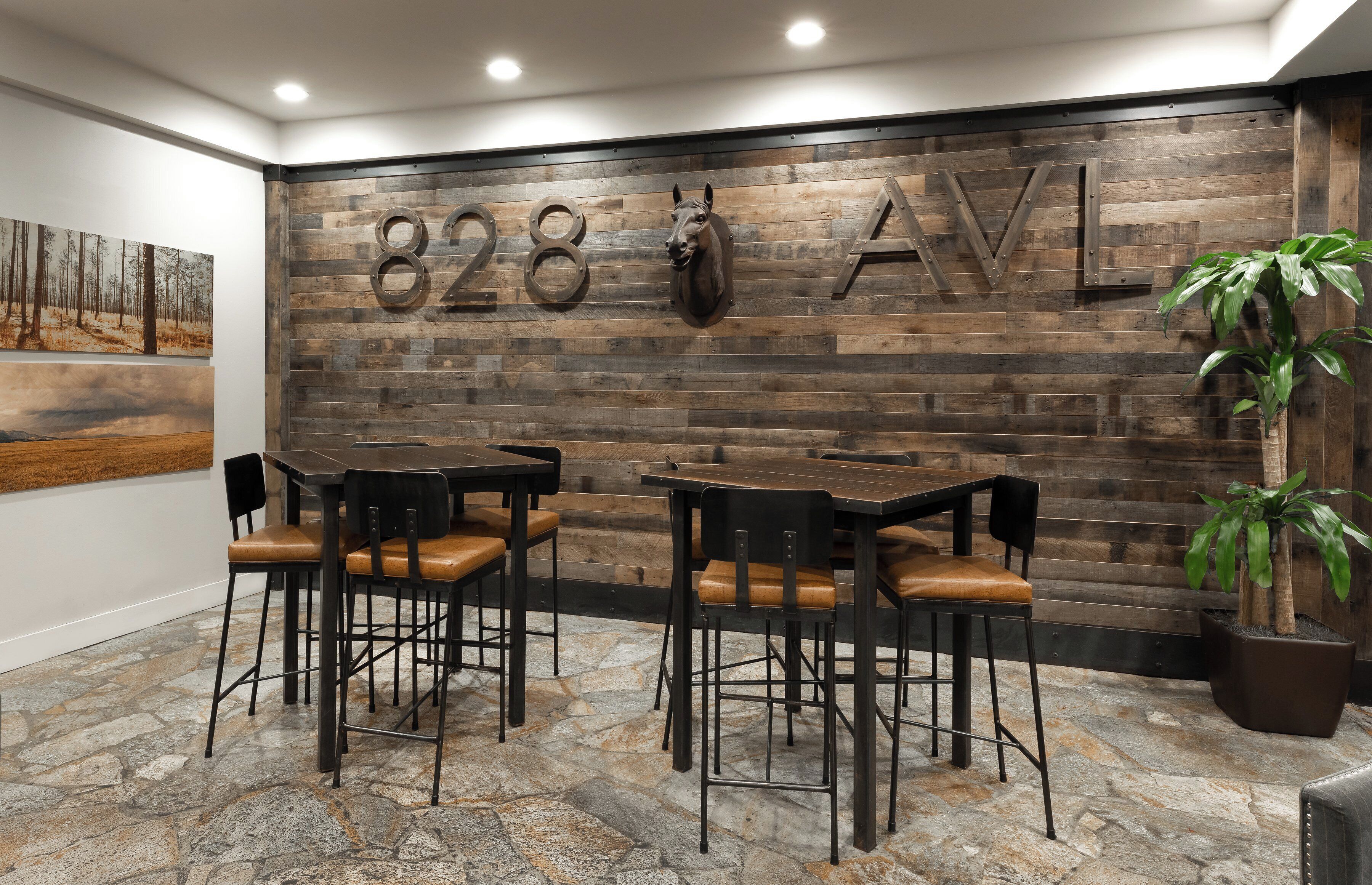 A modern interior with a wooden wall displaying the number '828 AVL', two tables with chairs, a potted plant, and a painting on the wall.