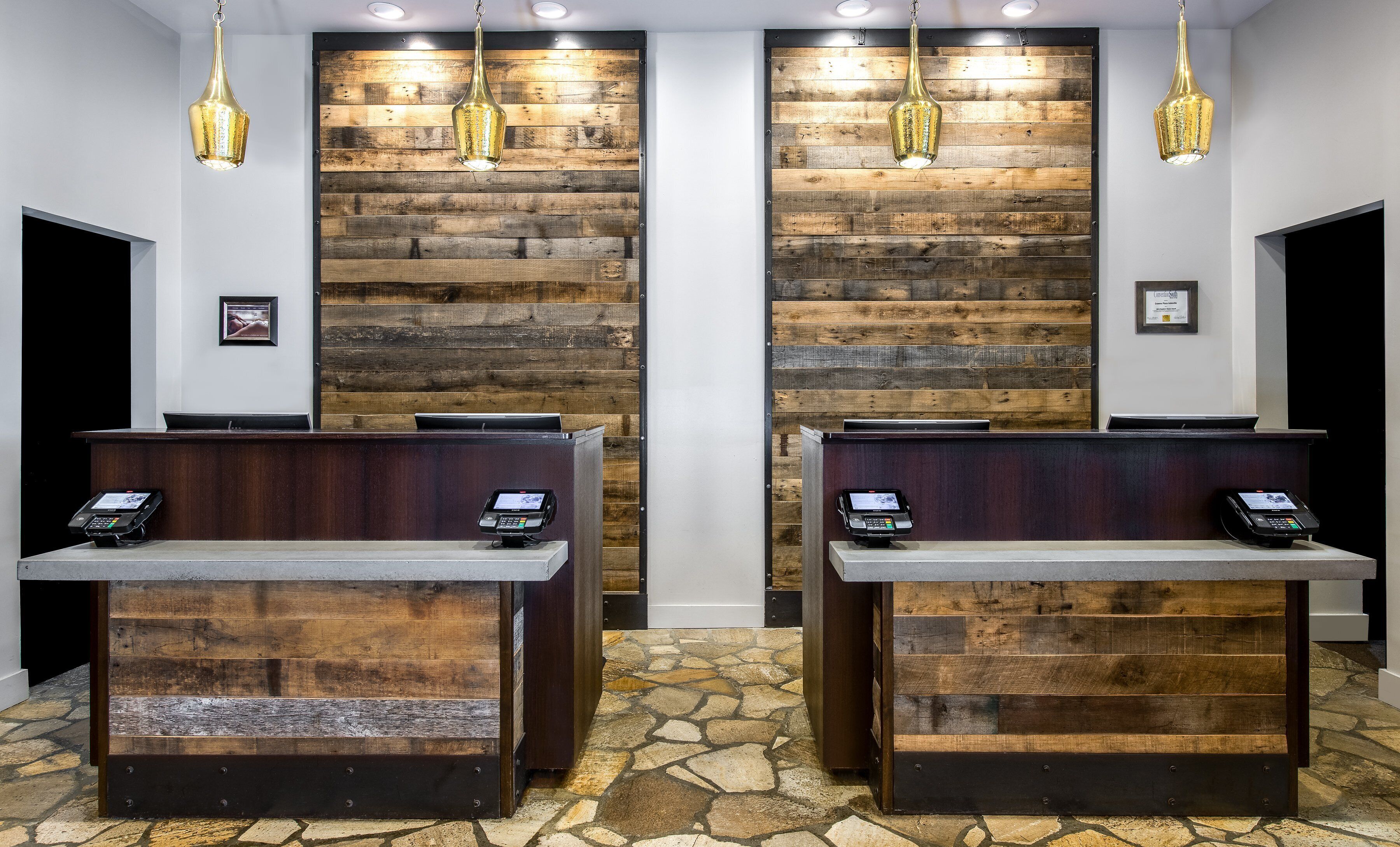 A reception area with two wooden reception desks, stone flooring, and hanging pendant lights.