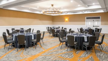 A conference room with multiple tables and chairs, a chandelier, and a carpeted floor.