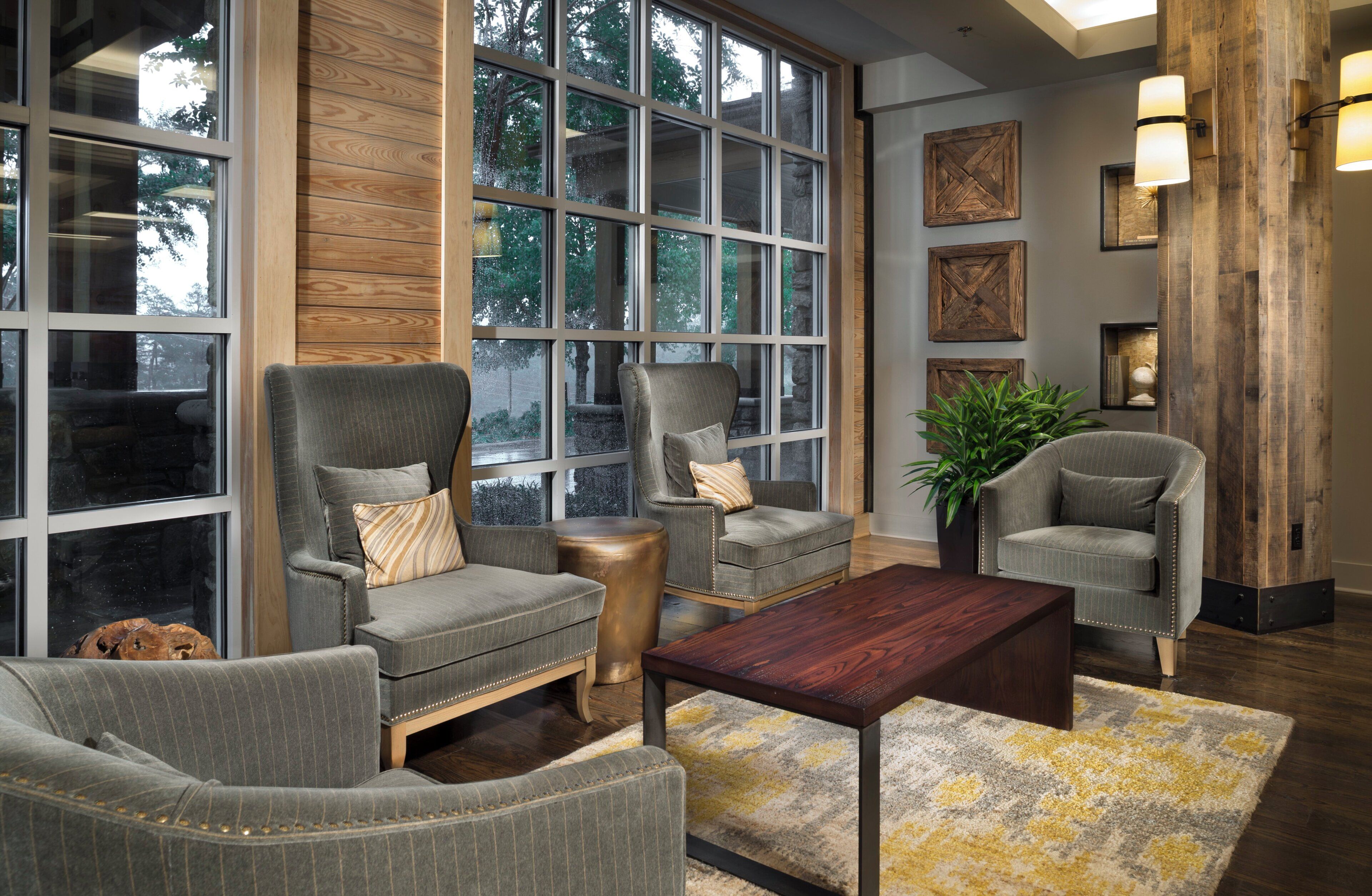 A modern living room with large windows, a wooden accent wall, and a mix of seating including armchairs and a sofa.