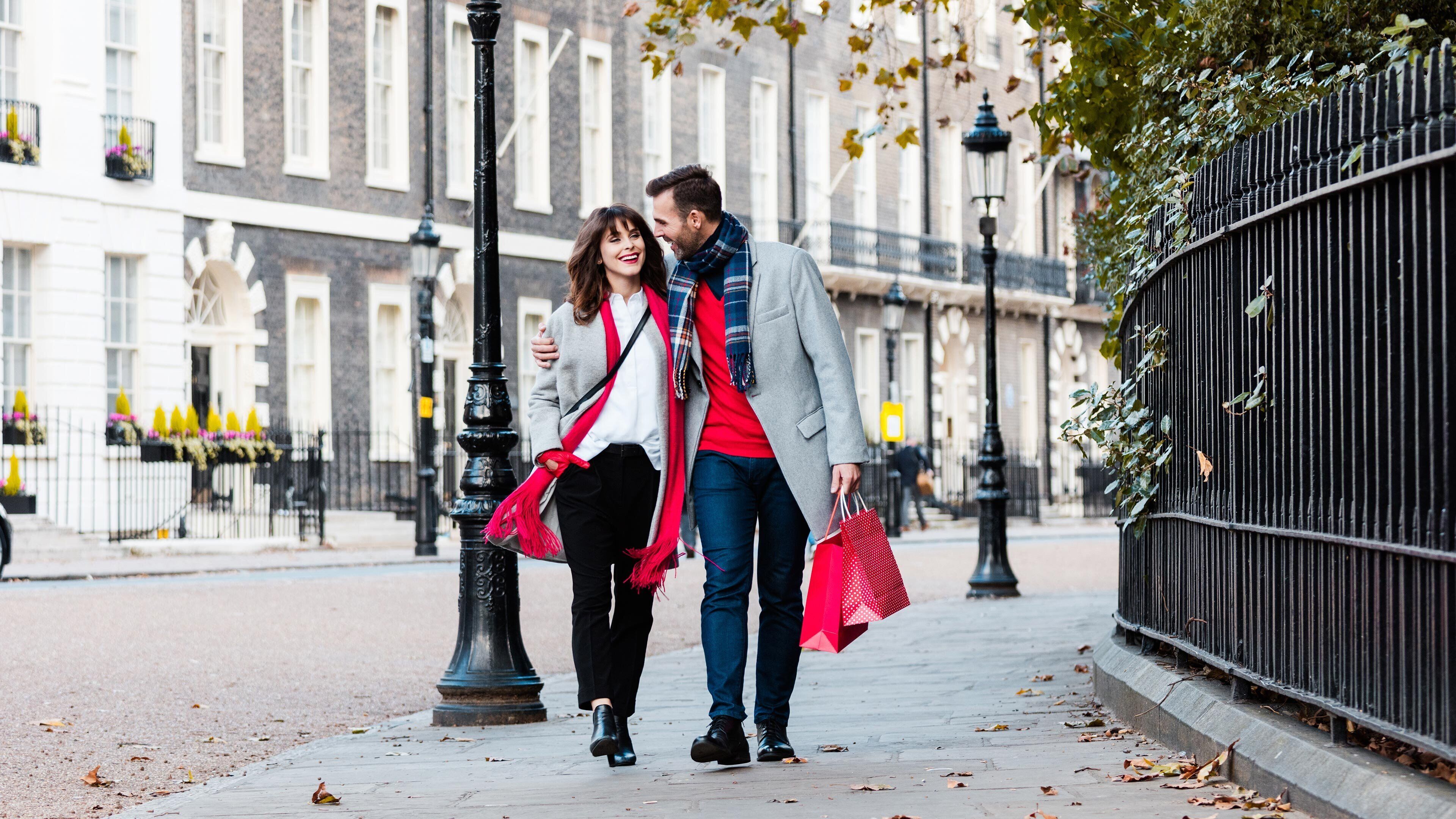 A couple walking on a city sidewalk with buildings in the background.