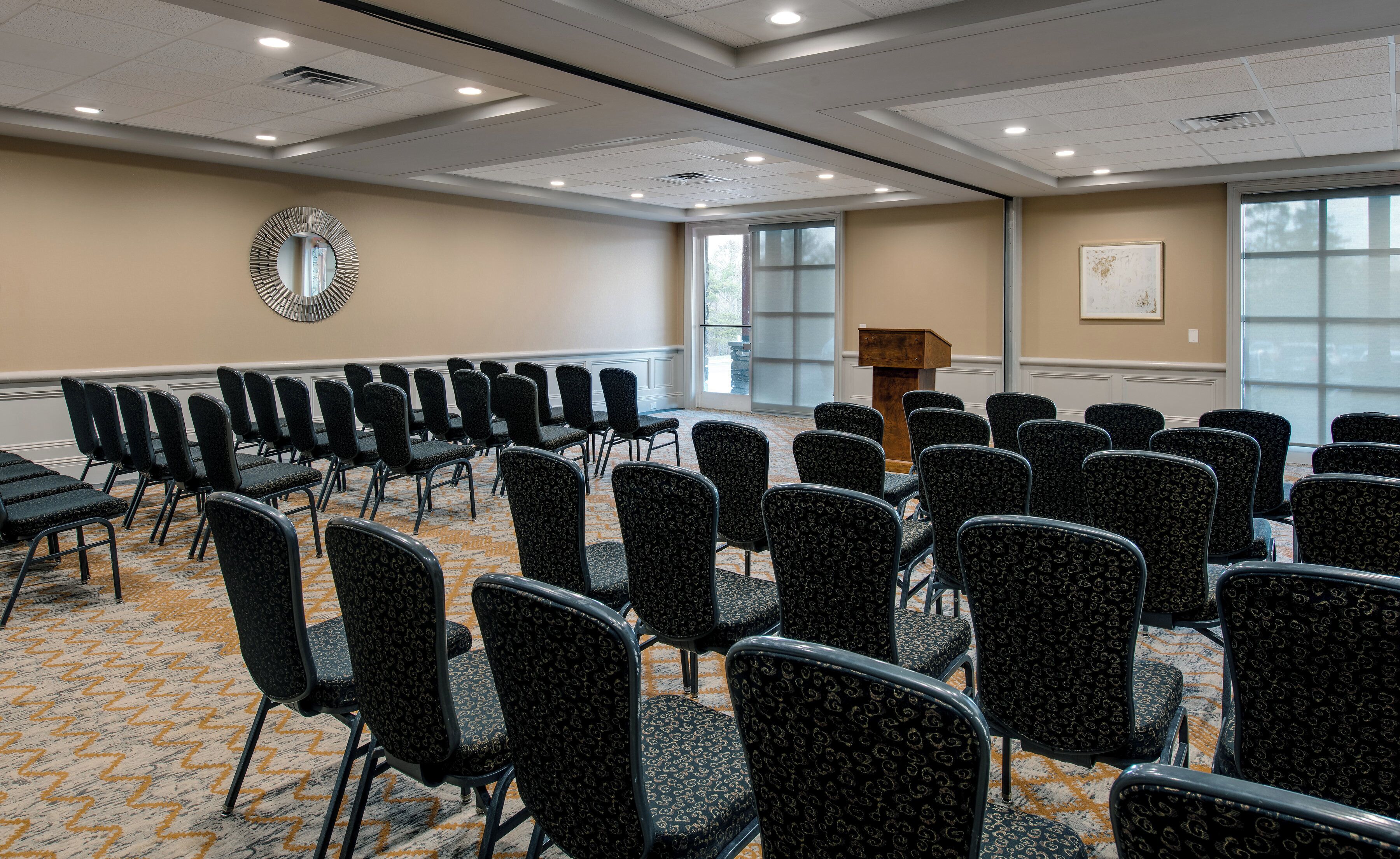 Une salle de conférence avec des rangées de chaises, un pupitre et une grande fenêtre.