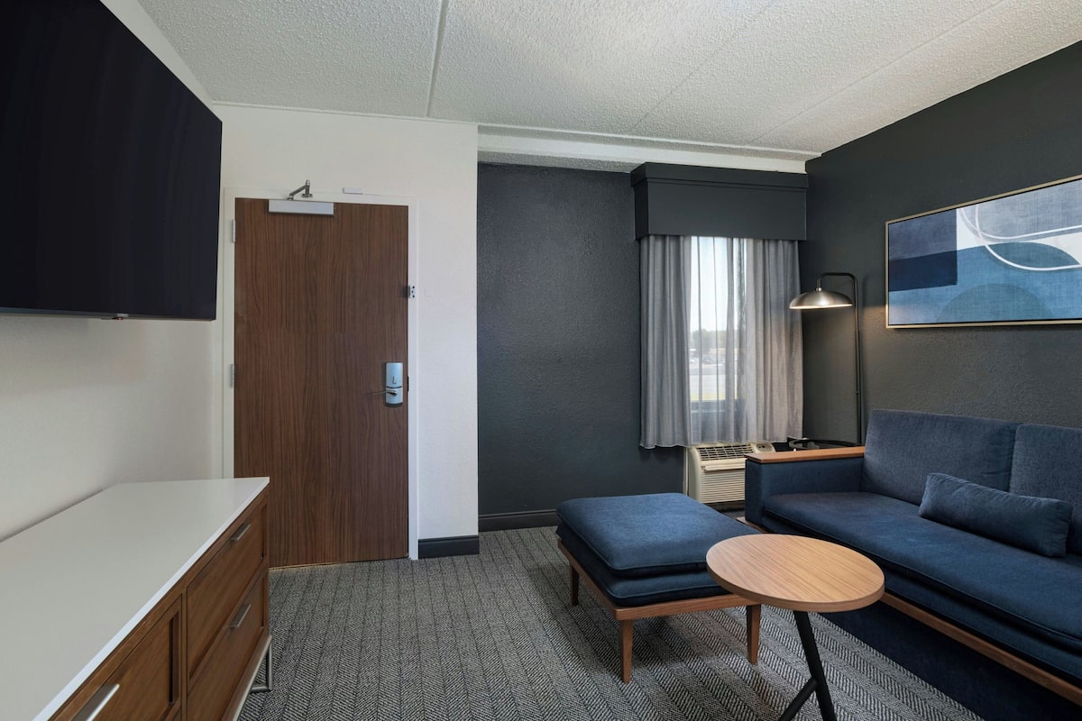 A modern hotel room with a sofa, a small table, a TV, and a door.