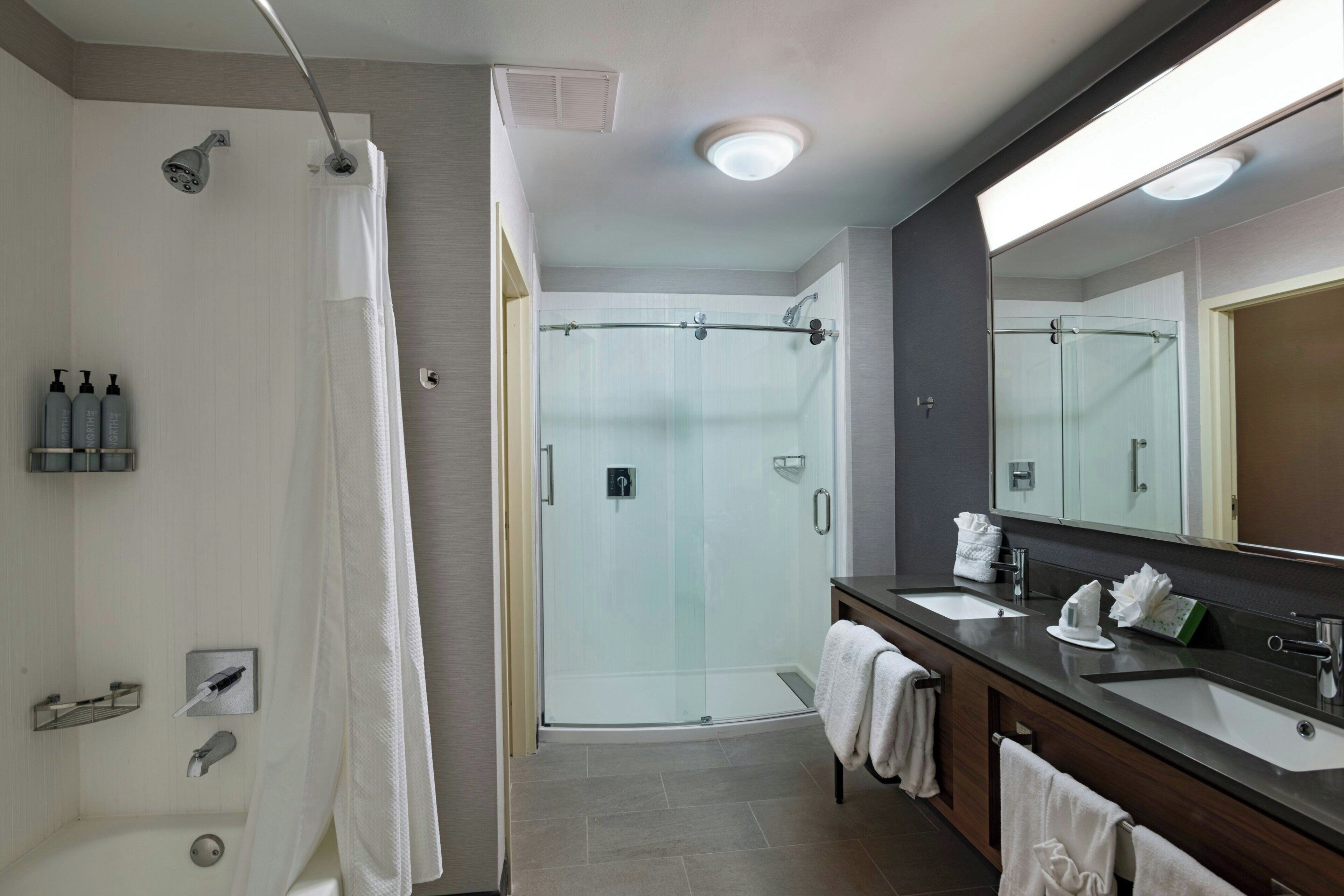Un baño moderno con ducha envuelta en vidrio, un espejo grande y un lavabo con encimera oscura.
